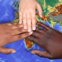 Drei Kinderhände liegen übereinander auf einem Globus