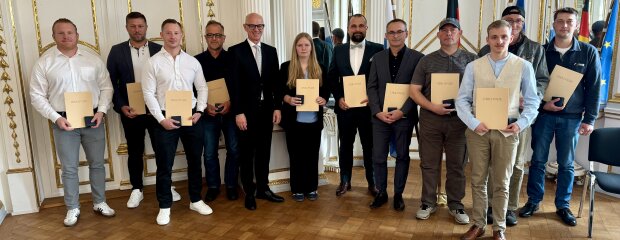 Gruppenfoto mit Regierungspräsident Walter Jonas und den elf Geehrten der Lebensretter-Ehrung in der Regierung der Oberpfalz, alle halten ihre Urkunden in den Händen.